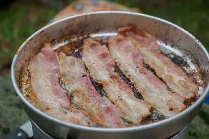 Bacon frying in a camping pan outdoors.