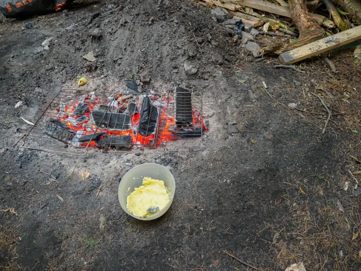 Glowing embers on a grill in a fire pit, with a bowl on the ground in front.