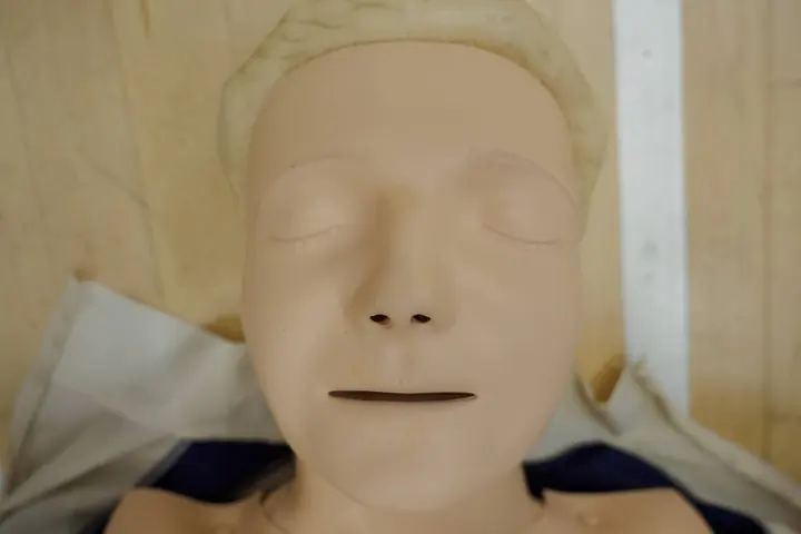 A first aid training manikin lying on a wooden floor.